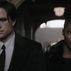 Bruce Wayne and Bella Real, both in black, walk down a church aisle at a funeral.
